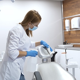 Une femme en tenue de ménage nettoie un siège dans une salle médicale, prêt pour les patients.